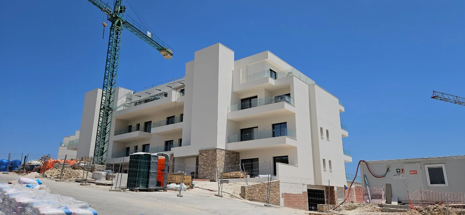 Bloque de viviendas con fachada blanca revestida, balcones y detalle de piedra en la planta baja