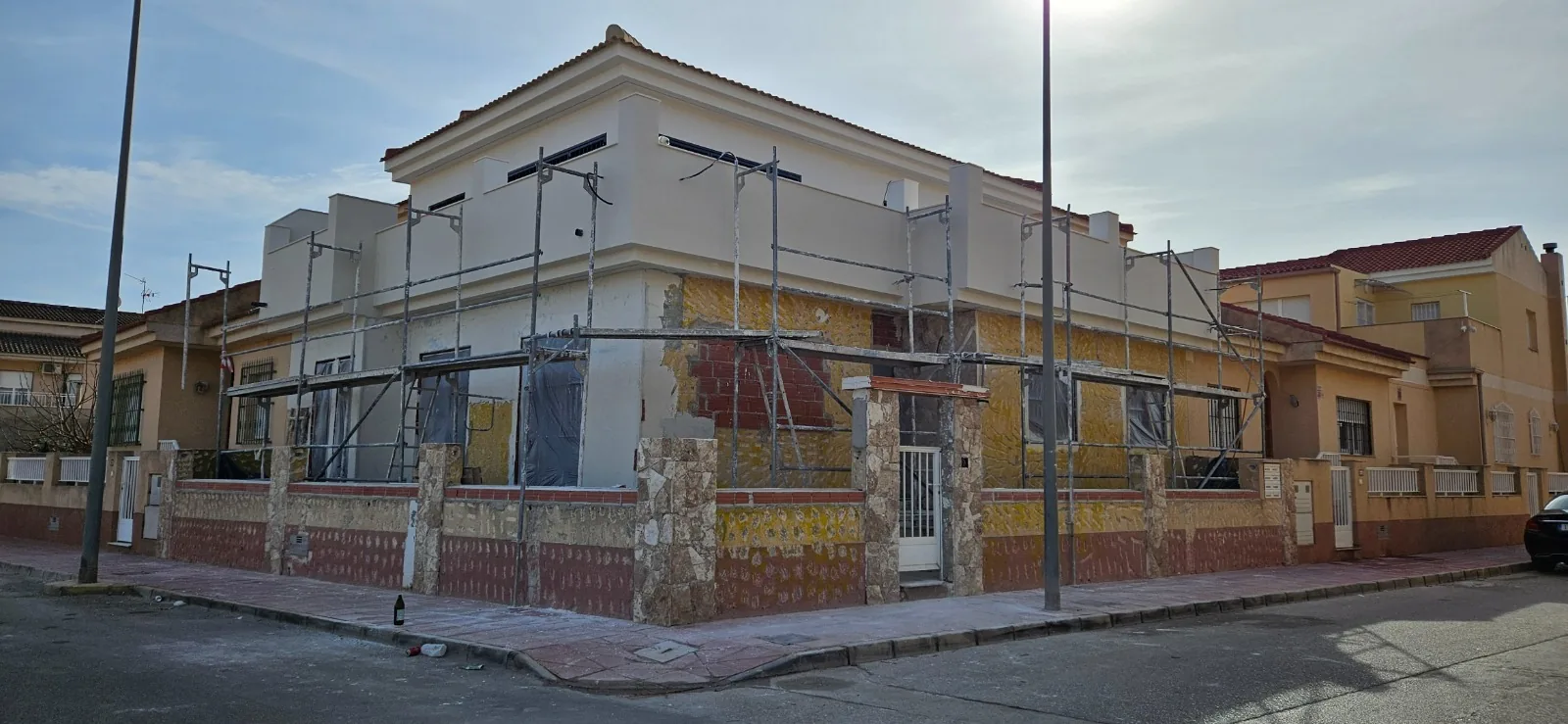 Vivienda de esquina con andamios y fachada en proceso de revestimiento, con zócalo de piedra y ladrillo