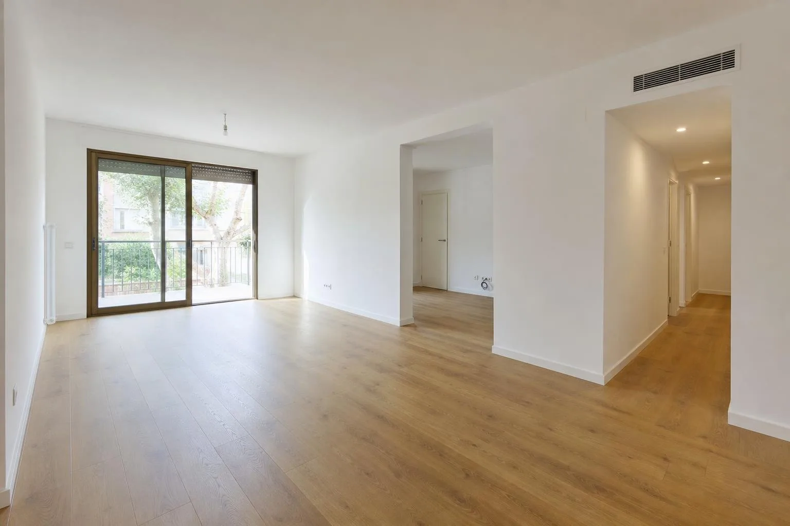 Salón reformado con paredes lisas, suelo nuevo y puerta de balcón