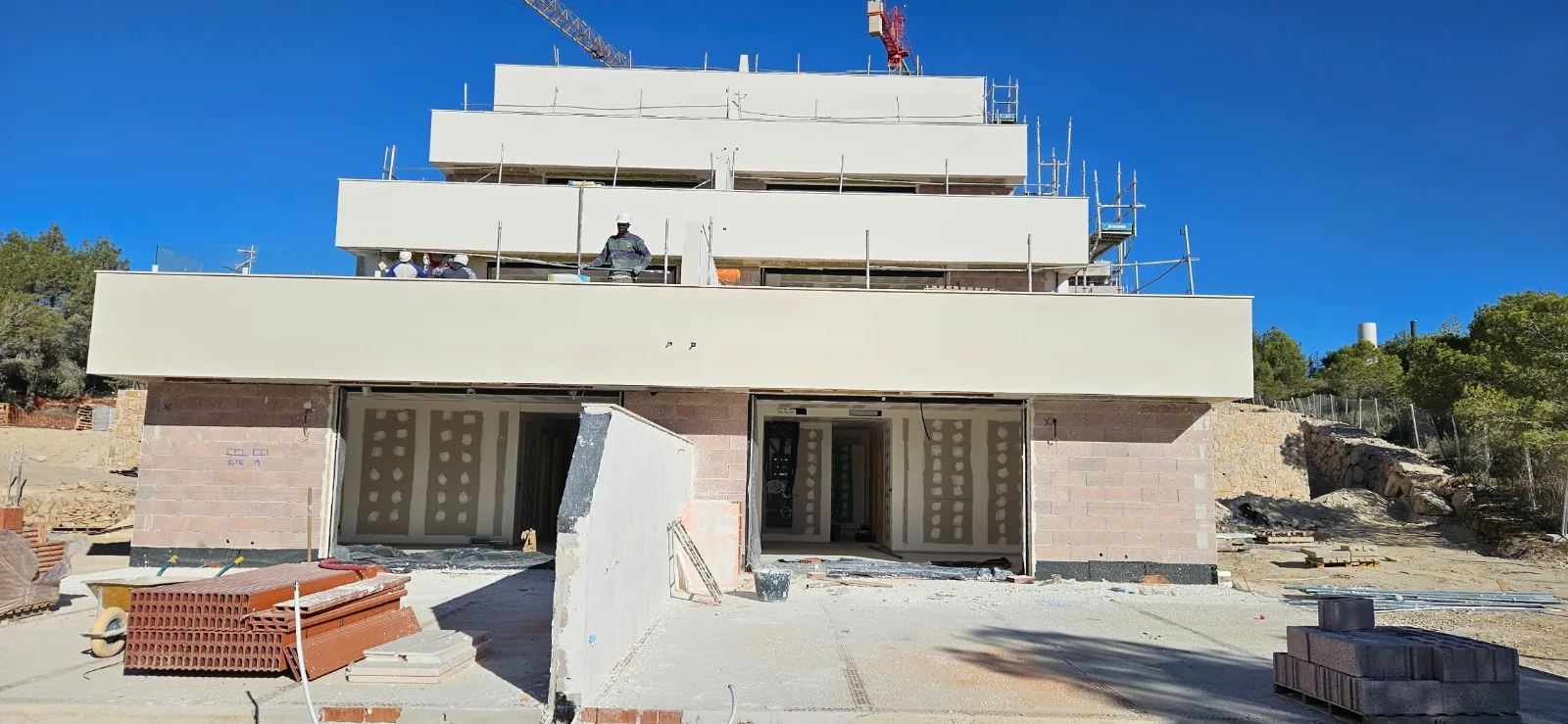 Edificio en construcción con fachada en terrazas escalonadas con monocapa blanco y grúa al fondo