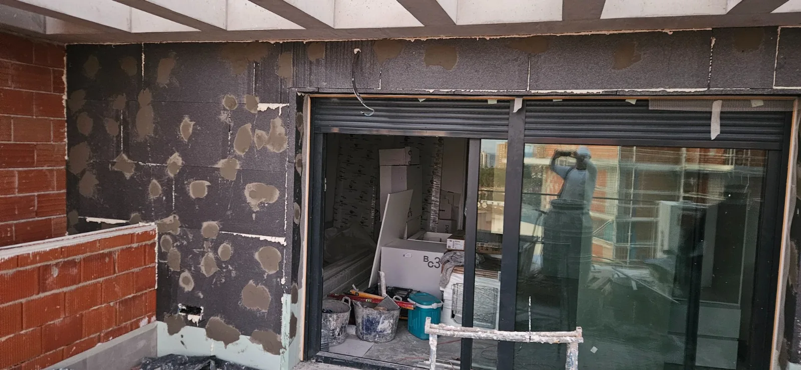 Pared exterior con paneles aislantes fijados con puntos de mortero junto a una cristalera