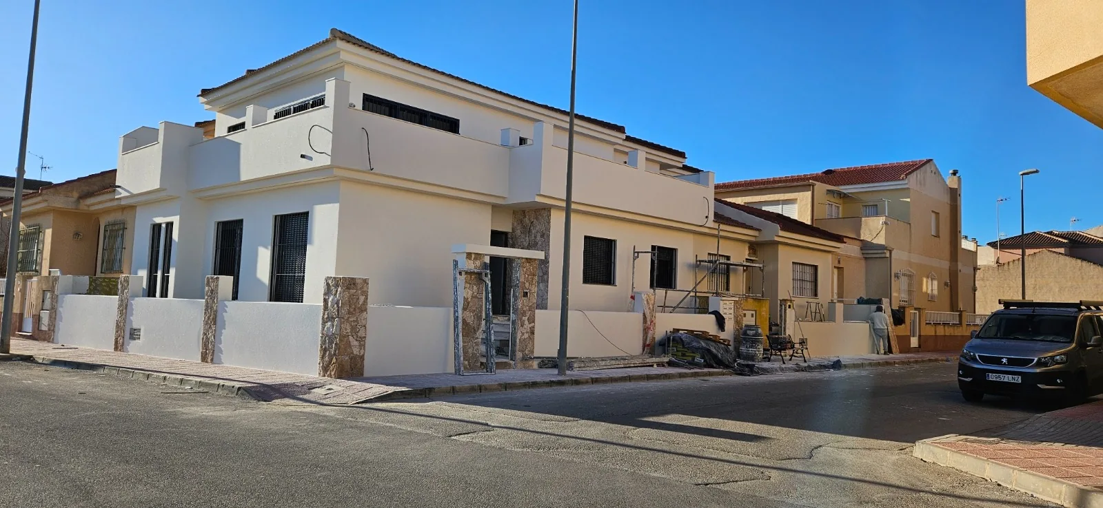 Vivienda de esquina con fachada blanca terminada, balcones y pilares revestidos de piedra