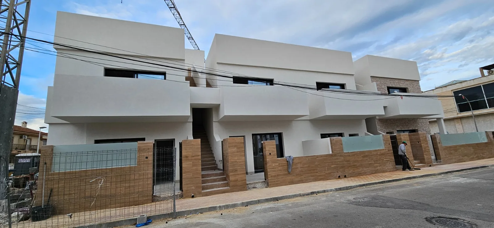 Conjunto de viviendas con fachada blanca terminada, escalera de entrada y vallas de ladrillo